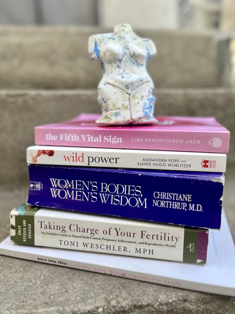 Stack of books on the ground with clay figurine in the shape of a women's body